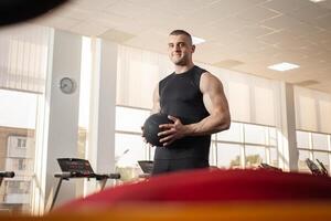 musclé entraîneur jette le Balle sur une trampoline, une muscle entraîneur, une salle de sport. portrait de une magnifique homme, encadrement, individuel poids perte et des sports cours. souriant photo