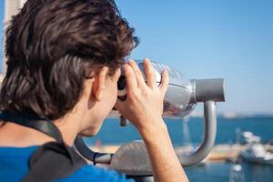 homme regards par Stationnaire jumelles. binoscope sur observation plate-forme près mer. port de mer dans Odessa. coûteux yachts sur le jetée. commercial machine, vente entreprise. photo