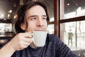 une homme les boissons café dans une café, une restaurant. intérieur, Naturel lumière du soleil, flou arrière-plan, de côté. collation, petit déjeuner. le déjeuner Pause. photo