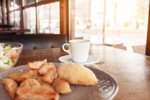 petit-déjeuner, dîner, le déjeuner dans une restaurant, café. cuit patates avec Boulettes de viande, César salade, café américain. intervieweur, délicieux nourriture, grand les fenêtres, Naturel lumière du soleil. flou Contexte photo