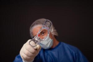 une gynécologue avec une Vénus miroir dans le sien mains. gynécologique accessoires, brosse, bâton. une médecin dans une médical masque, une peignoir, gants, avec une gynécologique miroir sur une gris Contexte. photo