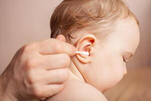 une homme nettoie le sien enfant oreilles. nettoyage une enfant oreille photo