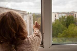 le enfant grimpe à le fenêtre, le fille sur le fenêtre seuil repose sur le filet, le danger de chute. le enfant est seul à maison, pouvez tomber en dehors de le la fenêtre. photo