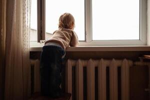 le enfant grimpe à le fenêtre, le fille sur le fenêtre seuil repose sur le filet, le danger de chute. le enfant est seul à maison, pouvez tomber en dehors de le la fenêtre. photo