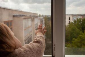 le enfant grimpe à le fenêtre, le fille sur le fenêtre seuil repose sur le filet, le danger de chute. le enfant est seul à maison, pouvez tomber en dehors de le la fenêtre. photo