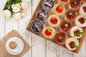 sucré dessert dans verre avec biscuit, baie fruit et fouetté crème. une tasse de thé, fleurs, Gâteaux dans une boîte. livraison de nourriture à le maison pour des soirées ou une dîner photo