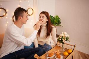 une Jeune content couple dans l'amour mange dans une photo studio. le gars et le fille sont marrant alimentation chaque autre. posant pour des modèles dans une studio pour Noël famille dîner pour Nouveau années veille, petit déjeuner dans lit