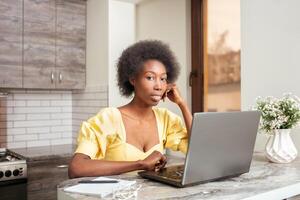 portrait de magnifique africain américain pigiste femme, table dans cuisine. travail sur ordinateur portable, intérieur. photo