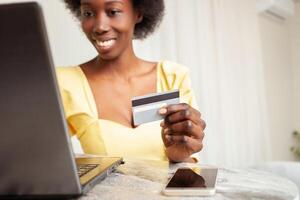magnifique africain américain noir femme les usages une banque carte à achats en ligne. livraison de des biens à maison. portable sur tableau. l'Internet photo