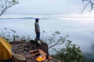 une Jeune Masculin voyageur des stands sur une Roche à une falaise rempli avec Matin brouillard dans le sien camp. photo