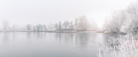 forêt d'hiver sur la rivière au coucher du soleil. paysage panoramique avec arbres enneigés, soleil, belle rivière gelée avec reflet dans l'eau. saisonnier. arbres d'hiver, lac et ciel bleu. rivière enneigée givrée. conditions météorologiques photo