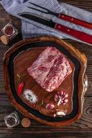 boeuf d'entrecôte cru sur une planche à découper en bois avec des épices et une fourchette et un couteau à barbecue - vue de dessus. photo