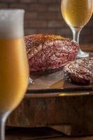 rumsteck tranché grillé avec deux verres de bière sur une planche à découper en bois. viande de boeuf en marbre - picanha brésilien. photo