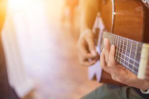 une Jeune homme est pratiquant en jouant guitare dans une la musique entraine toi pièce avant performant dans commande à réduire le erreur de en jouant guitare sur organiser. proche en haut Jeune homme est en portant guitare accords pour entraine toi. photo