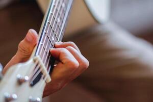 une Jeune homme est pratiquant en jouant guitare dans une la musique entraine toi pièce avant performant dans commande à réduire le erreur de en jouant guitare sur organiser. proche en haut Jeune homme est en portant guitare accords pour entraine toi. photo