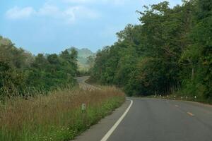 asphalte route cette courbes retour et de suite. côté de le route a été couvert avec herbe et vert des arbres le long de le flanc de montagne. en dessous de bleu ciel. route à pong district, phayao Province route de Thaïlande. photo