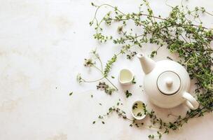 ai généré une blanc thé pot sur Haut de une blanc surface avec herbes photo