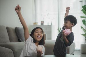 peu asiatique fille et garçon économie argent dans une porcin banque, apprentissage à propos économie, le enfant sauve argent pour futur éducation. argent, finances, assurance, et gens concepts. photo