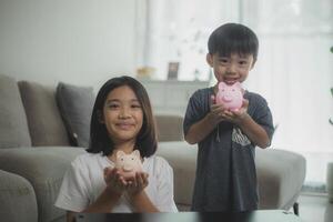 peu asiatique fille et garçon économie argent dans une porcin banque, apprentissage à propos économie, le enfant sauve argent pour futur éducation. argent, finances, assurance, et gens concepts. photo