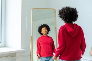 l'amour toi-même. magnifique Jeune souriant africain américain femme dansant profiter sa miroir réflexion. noir Dame à la recherche à miroir à la recherche sur de soi et heureux. soi l'amour concept photo