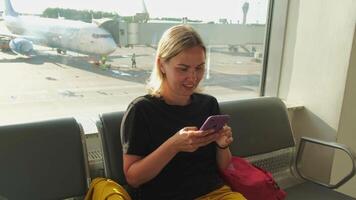 aéroport Terminal. femme attendre pour vol en utilisant téléphone intelligent. fille avec cellule téléphone dans aéroport surfant l'Internet social médias applications. en voyageant femelle dans embarquement salon de Compagnie aérienne moyeu. en voyageant fille photo