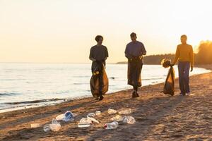 Terre journée. bénévoles militants équipe recueille des ordures nettoyage de plage côtier zone. femme mans avec poubelle dans des ordures sac sur océan rive. environnement préservation côtier zone nettoyage photo