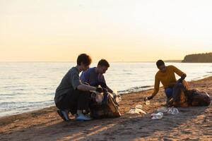 Terre journée. bénévoles militants recueille des ordures nettoyage de plage côtier zone. femme et mans met Plastique poubelle dans des ordures sac sur océan rive. environnement préservation côtier zone nettoyage photo