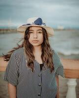 portrait de attrayant femme dans chapeau sur le jetée à la recherche à caméra. portrait de Jeune touristique femme dans chapeau sur une jetée photo