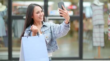 l'acheteur asiatique utilise un smartphone pour prendre un selfie. elle se leva et tenait un sac à provisions. photo