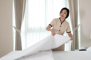 jeune et belle femme de chambre asiatique arrangeant une couverture sur le lit dans une chambre d'hôtel photo