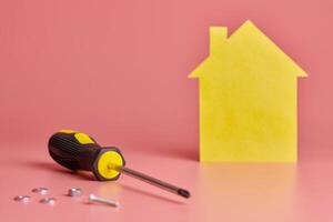 réparation à domicile et concept redécoré. rénovation de la maison. vis et figure en forme de maison jaune sur fond rose. photo