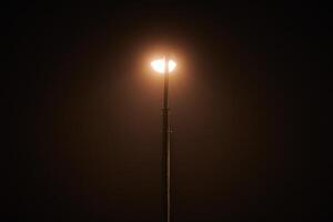 un lampadaire de nuit brille d'une faible lumière jaune mystérieuse à travers le brouillard du soir photo