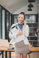 amical Jeune femme d'affaires engagé dans une téléphone appel tandis que en portant documents, permanent dans une bien éclairé Bureau espace. photo