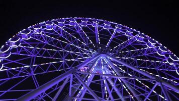 ferris roue dans bleu néon lumière sur foncé arrière-plan, partie de ferris roue avec bleu éclairage contre une noir ciel Contexte à nuit. ferris roue par nuit. ferris roue avec multicolore photo