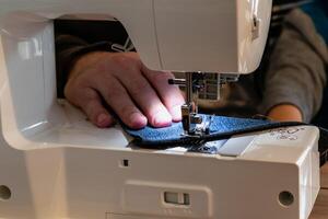 homme en utilisant une couture machine avec une bleu vêtement, pour réparation travail, personnalisation, création, recyclage photo