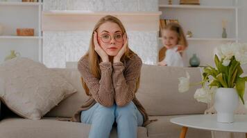 fatigué dérangé caucasien mère séance sur canapé à Accueil triste frustré stressé épuisé fatigué maman souffrir mal de crâne avec actif bruit difficile enfant enfant bébé fille fille fonctionnement autour en jouant photo