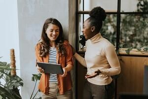 deux Jeune affaires femmes avec numérique tablette permanent dans le moderne Bureau photo