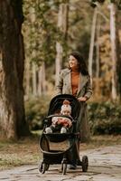 Jeune femme avec mignonne bébé fille dans bébé poussette à le l'automne parc photo