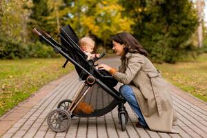 Jeune femme avec mignonne bébé fille dans bébé poussette à le l'automne parc photo