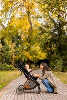 Jeune femme avec mignonne bébé fille dans bébé poussette à le l'automne parc photo