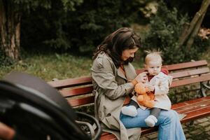 Jeune femme séance sur une banc avec mignonne bébé fille dans le l'automne parc photo