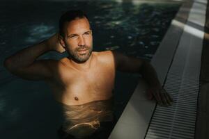 Beau Jeune homme relaxant sur le bord de intérieur nager bassin photo