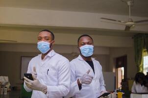 deux africain médecins dans le laboratoire se sent excité à propos elles ou ils vu sur leur téléphone portable et fait les pouces en haut photo