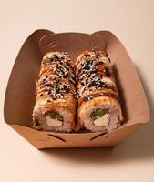 asiatique Sushi. Sushi avec anguille, sauce et sésame dans une papier récipient sur une lumière Contexte. nourriture livraison. photo