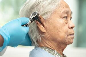 audiologiste ou ent médecin utilisation otoscope vérification oreille de asiatique Sénior femme patient traiter audition perte problème. photo