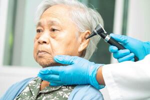 audiologiste ou ent médecin utilisation otoscope vérification oreille de asiatique Sénior femme patient traiter audition perte problème. photo