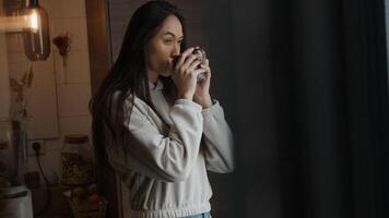 Jeune femme métisse tient la tasse dans les mains, regardant à travers la fenêtre de manière contemplative photo