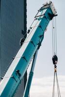 bleu grue levage mécanisme avec crochets près le verre moderne bâtiment, grue et hydraulique haute ascenseur en haut à 120 mètres photo