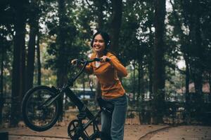 content Jeune asiatique femme tandis que équitation une vélo dans une ville parc. elle sourit en utilisant le vélo de transport. écologiquement amical concept. photo