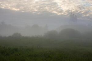 paysage brumeux du matin d'été avec l'église sur la colline en arrière-plan photo